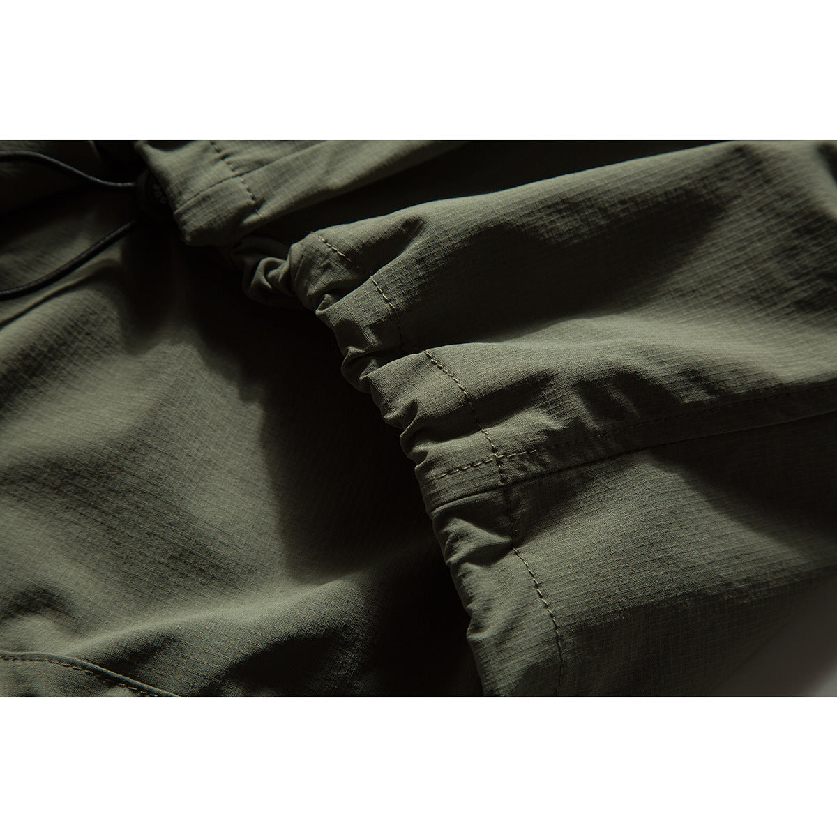 Close-up of the olive garment's sleeve and stitched seams, showing its textured surface and dark piping.