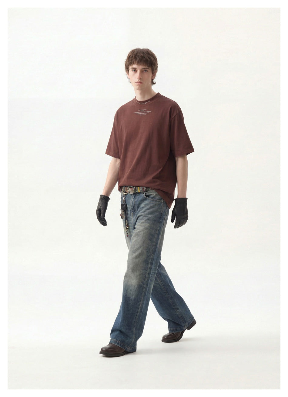 Full-length model wearing a burgundy oversized T-shirt, loose blue jeans, black gloves, and dark shoes.