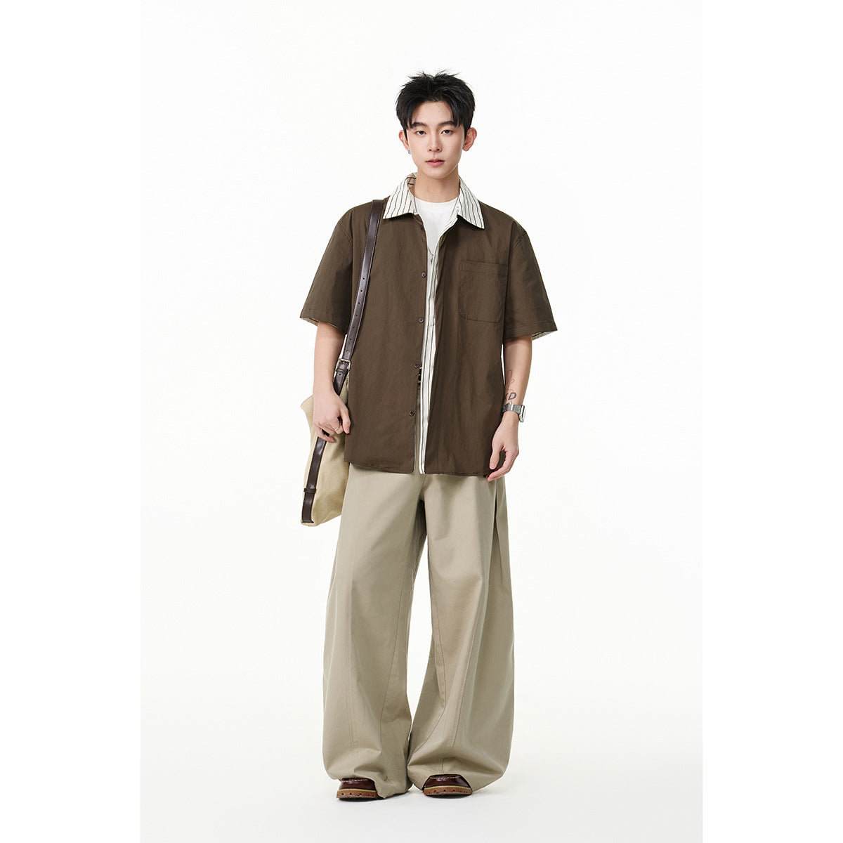 Model wearing a dark brown short-sleeve button-up shirt with a striped collar, paired with loose beige trousers.