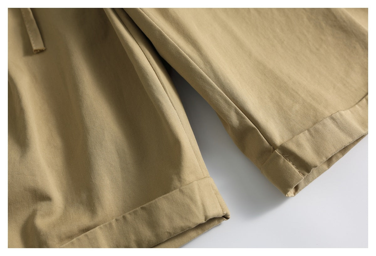 Close-up of tan shorts showing two wide folded leg hems and a glimpse of the drawstring.