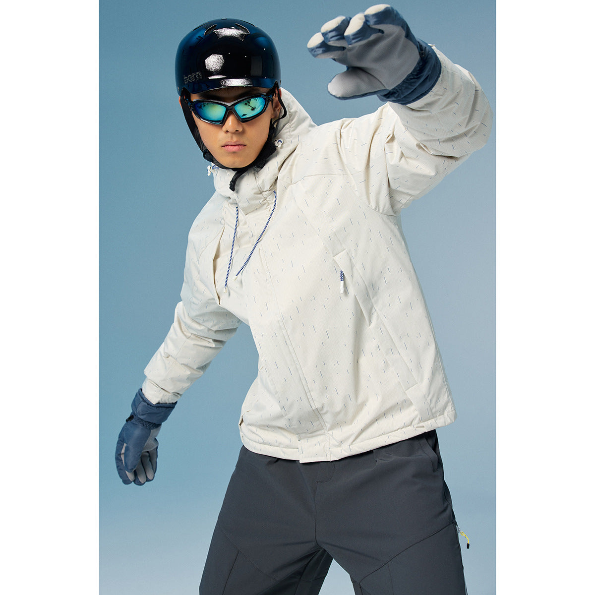 Man models a white speckled hooded jacket with blue zipper details and dark snow pants.