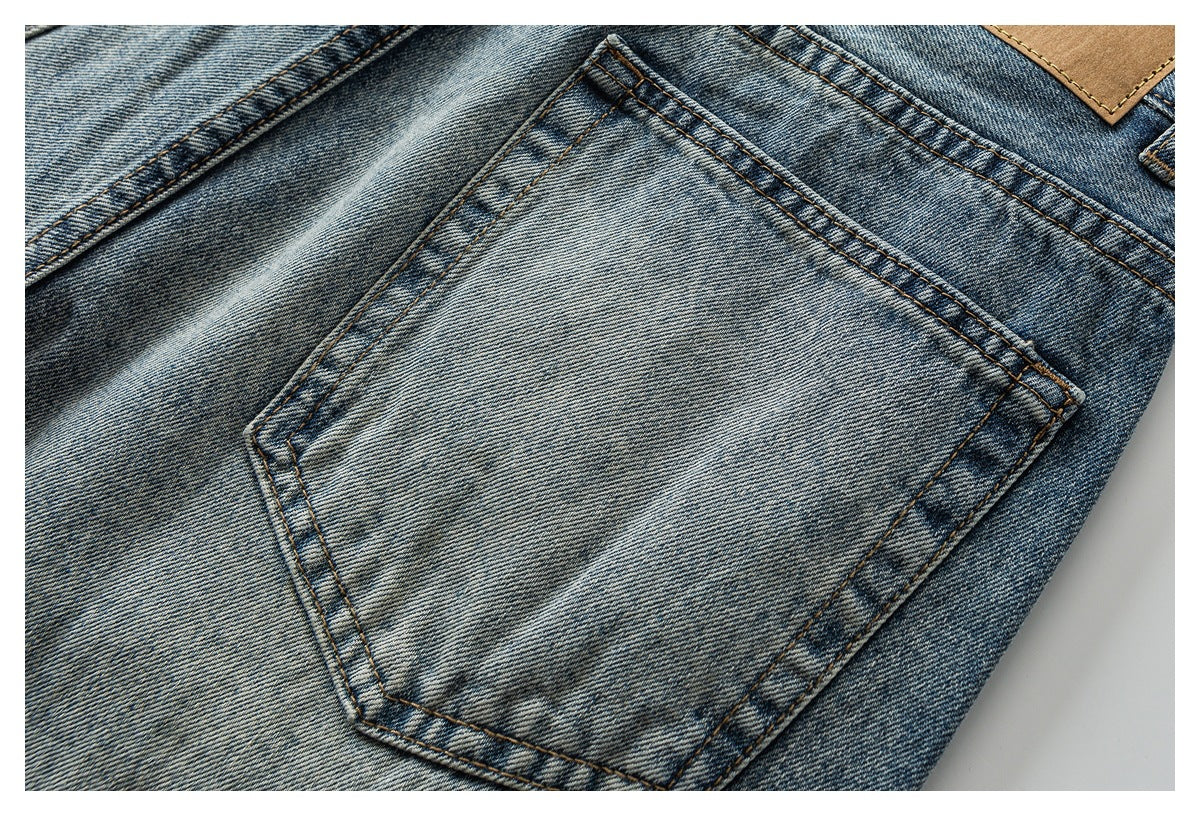 Close-up of faded blue denim with a stitched back pocket and tan leather patch.