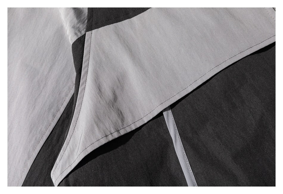 Close-up of a gray and black color-block garment with overlapping panels and visible stitching.