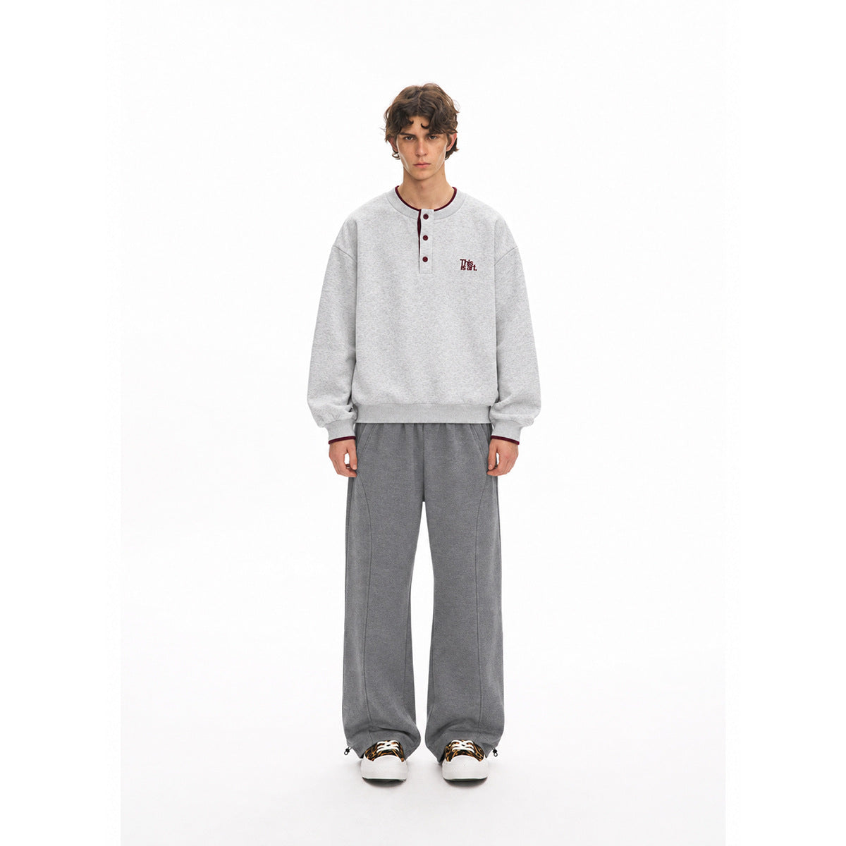 Full-length front view of a model wearing a light gray button-neck sweatshirt and wide-leg dark gray pants.