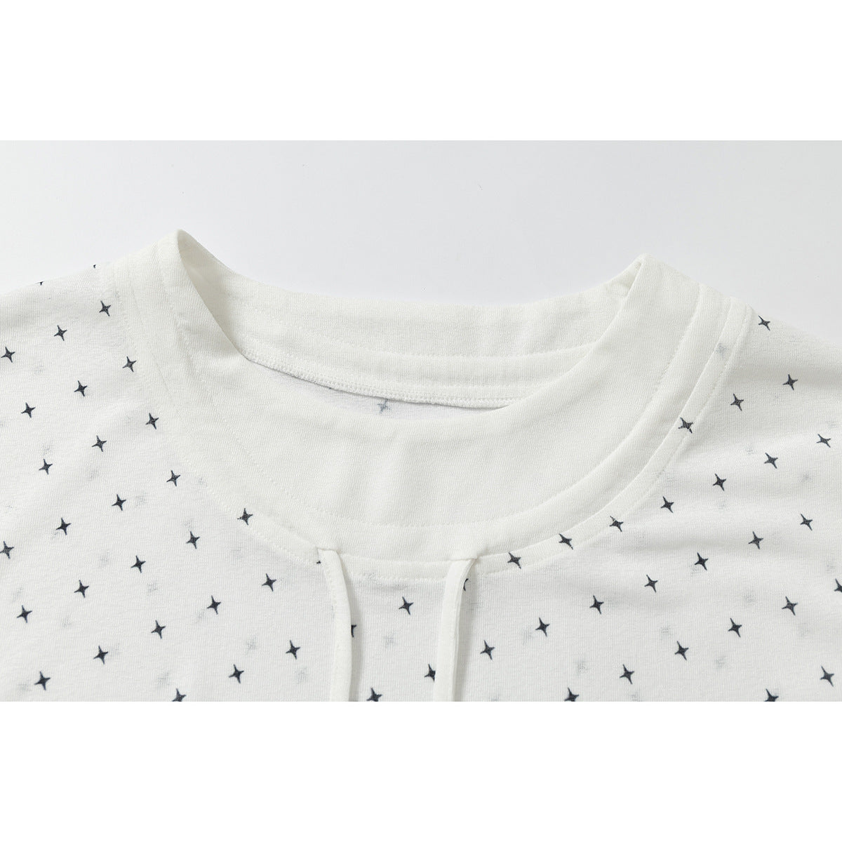 Close-up of a white top with scattered black stars, showing the round neckline and front opening.