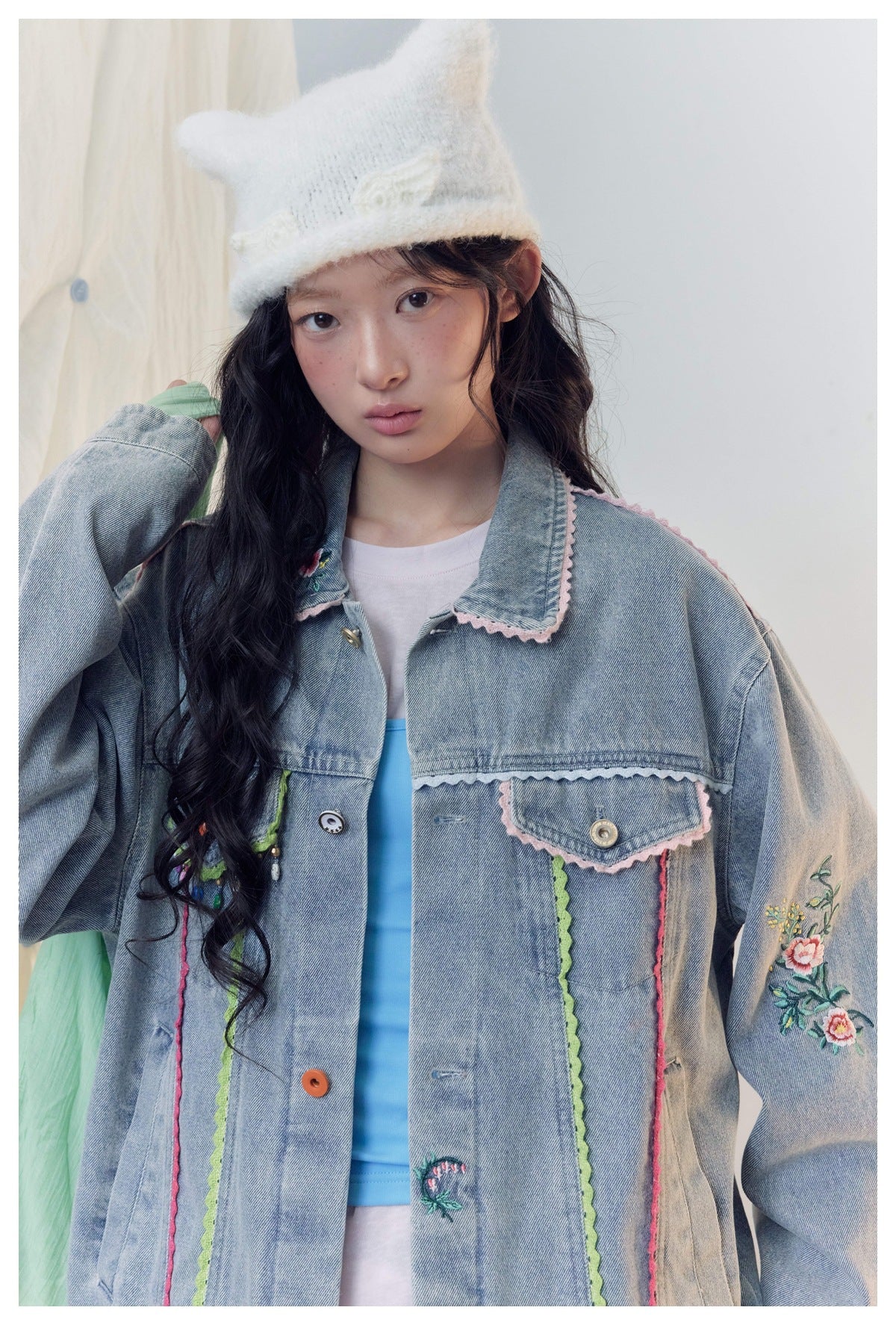 Close view of a model wearing a light-blue denim jacket with pink and green trim and floral sleeve embroidery.