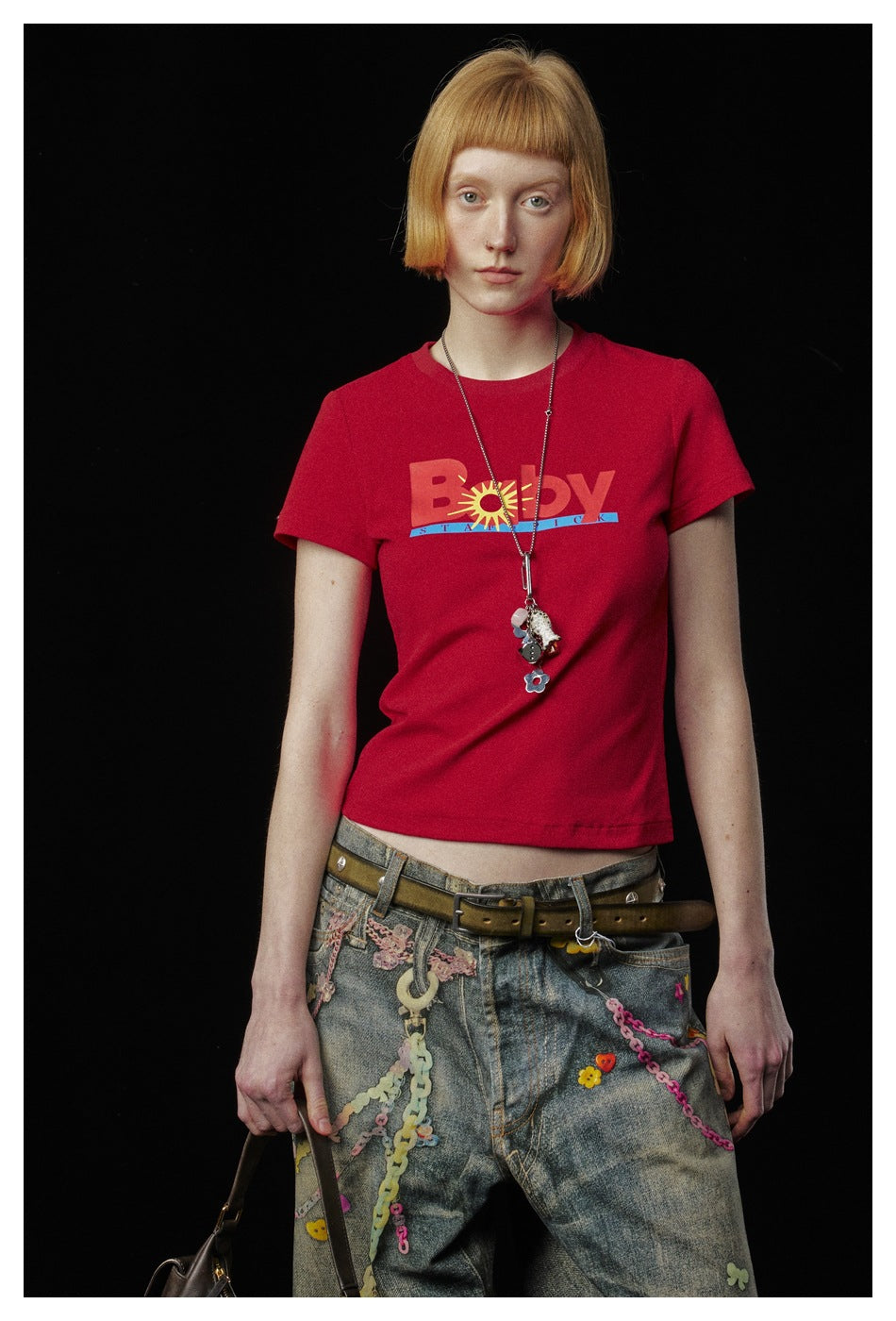 Model wearing a red cropped crew-neck T-shirt with a colorful chest graphic, paired with embellished jeans.