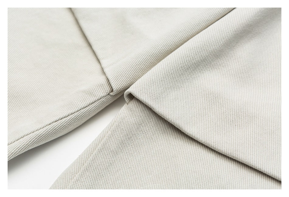 Close-up of overlapping off-white trouser fabric with a stitched seam and folded edge.
