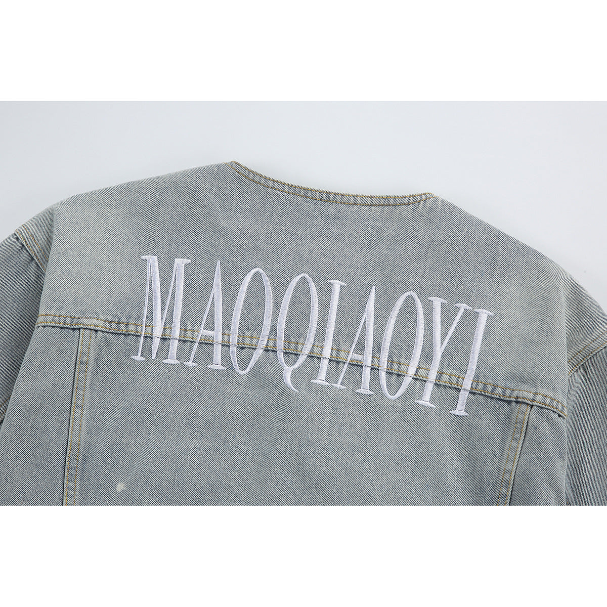 Close-up of the back of a light-wash denim jacket with large white embroidered lettering.