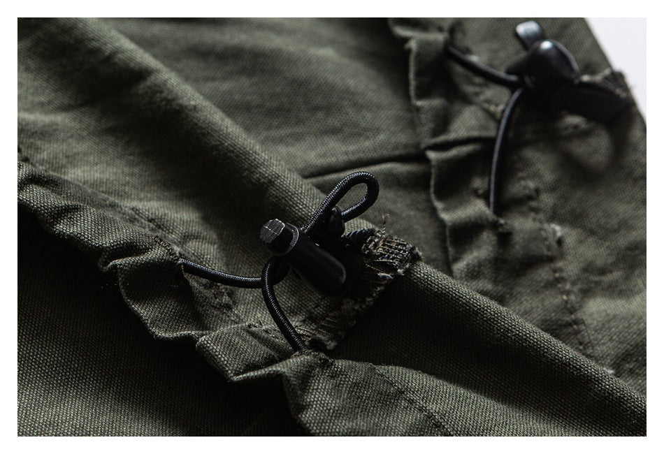 Close-up of olive trousers showing a black adjustable drawcord toggle.