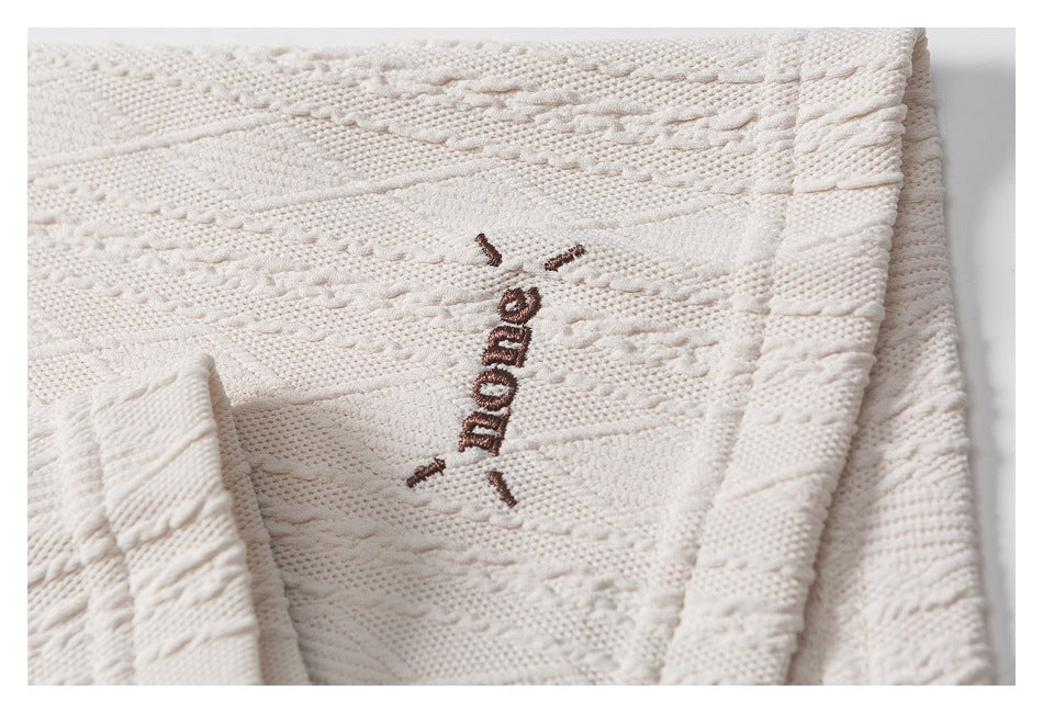 Close-up of brown embroidered lettering on the cream polo's textured fabric.