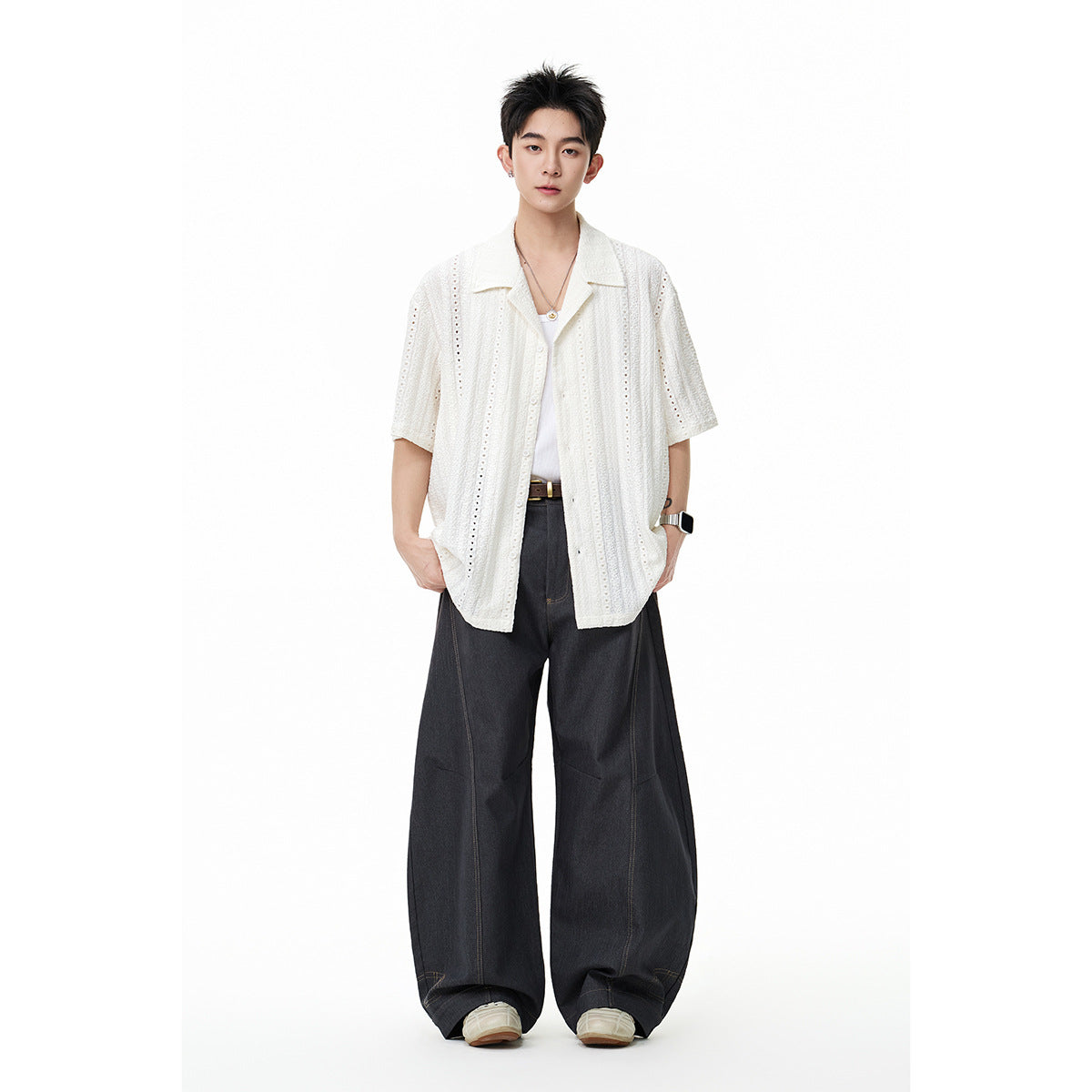 Model wearing a white short-sleeve eyelet shirt with wide black trousers, shown full length against a white background.