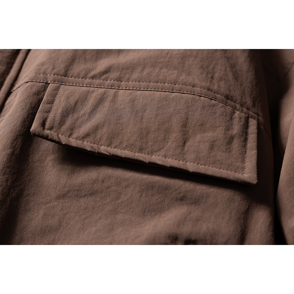 Close-up of a brown jacket's rectangular flap pocket and stitching.