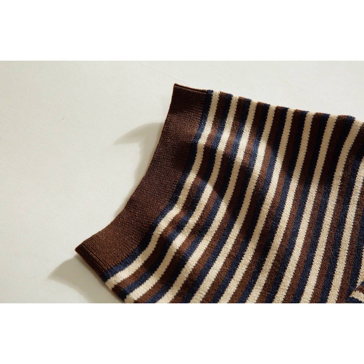Close-up of a brown ribbed sleeve cuff against cream, brown, and navy striped knit fabric.