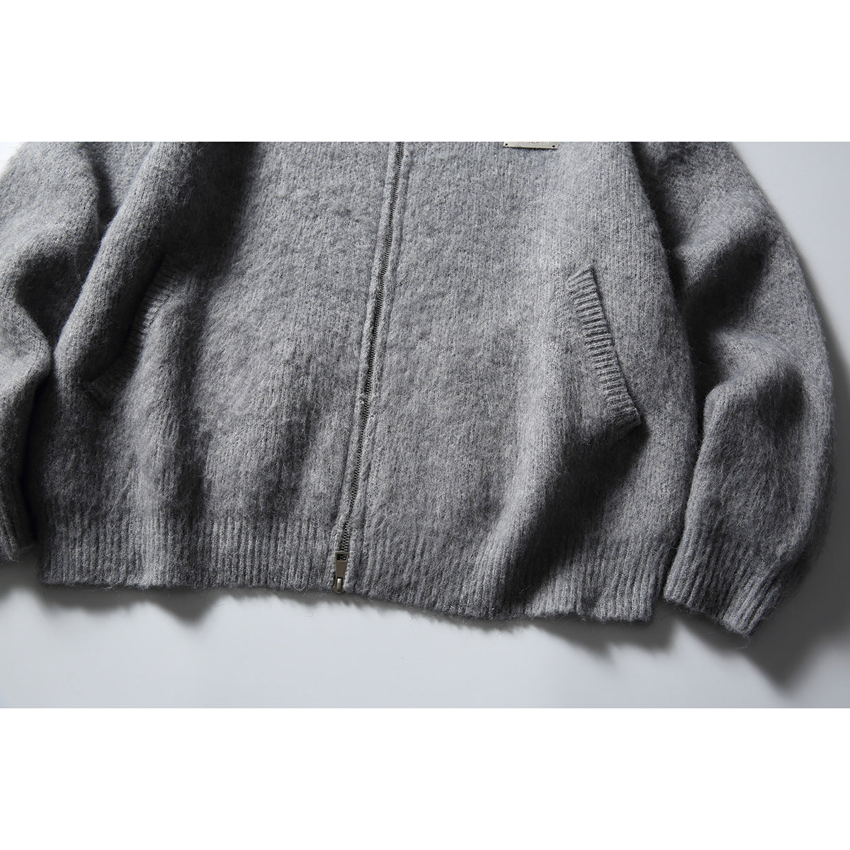 Close-up of a gray zip-front hooded sweater showing its pockets, cuffs, and ribbed hem.