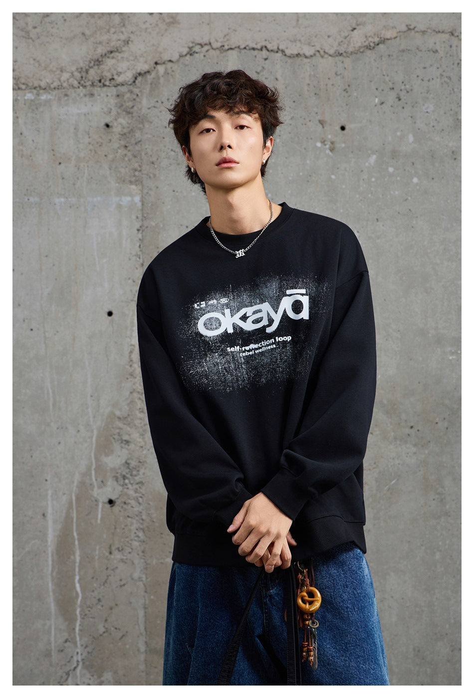 Model wearing a black oversized crewneck sweatshirt with a distressed white chest graphic and blue jeans.