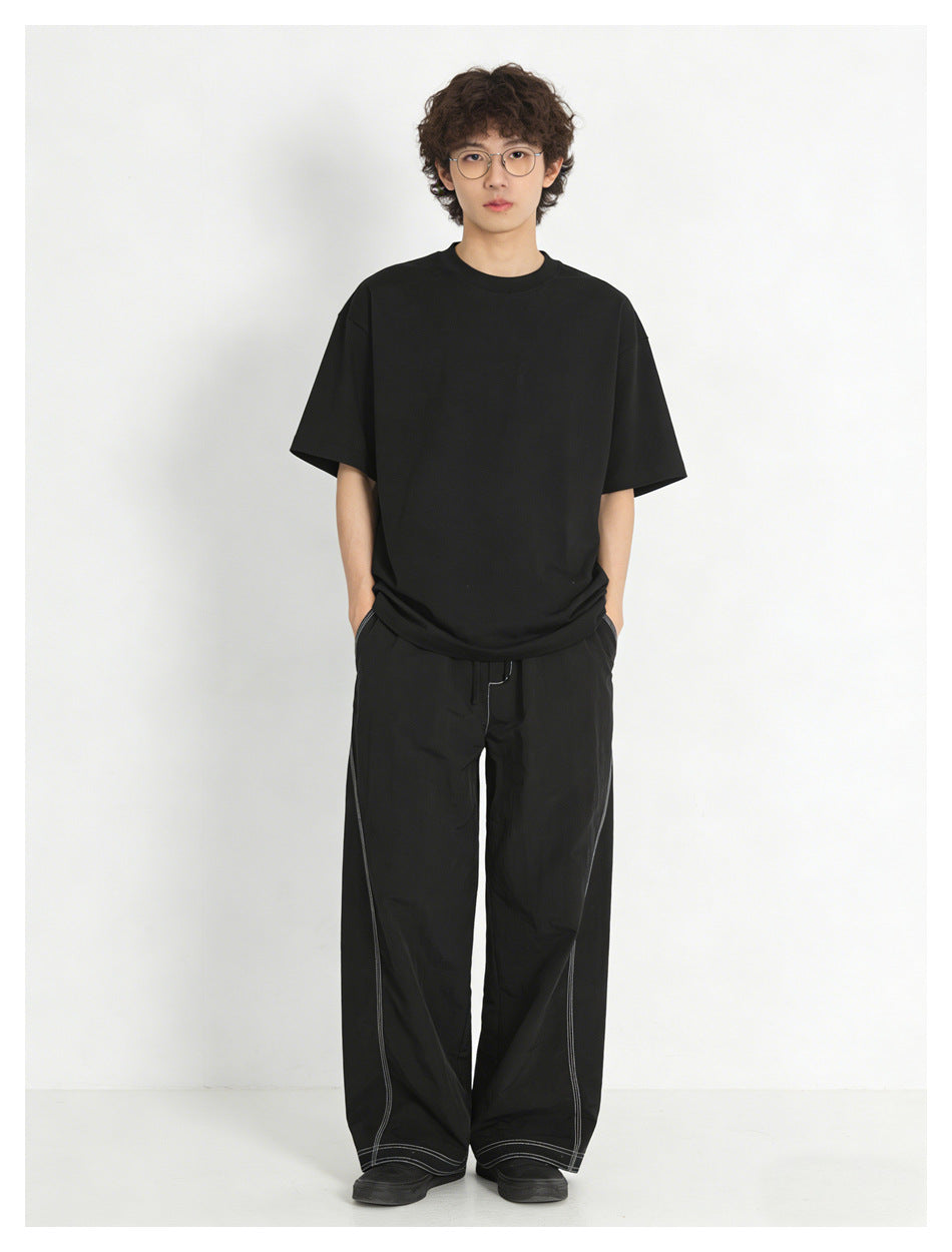 Model wearing a plain black T-shirt and loose black wide-leg pants with contrasting light stitching.