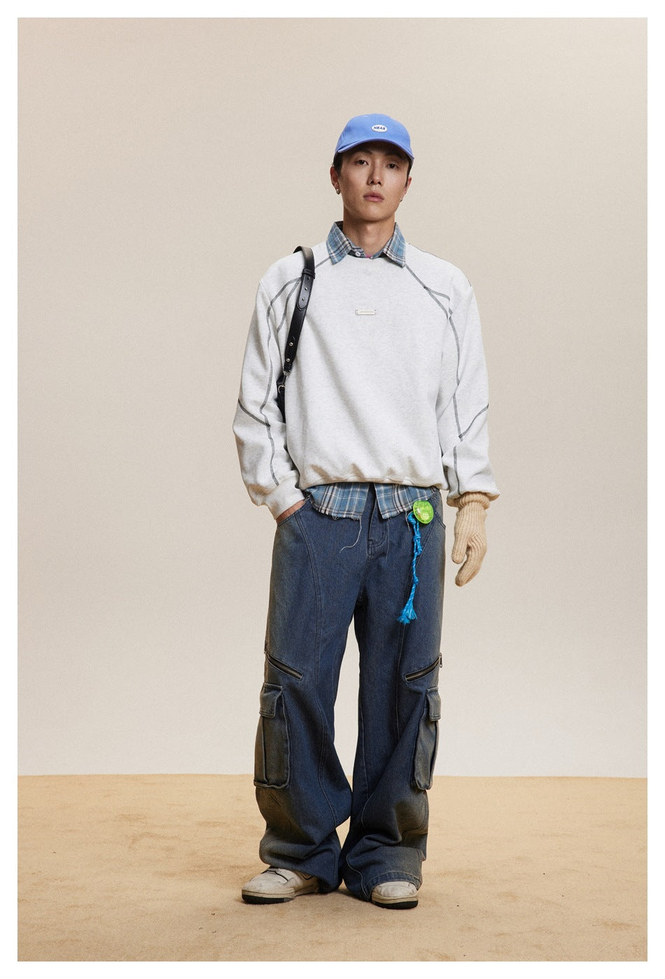 Full-length model wearing a light gray crewneck sweatshirt with dark contrast seams over a plaid shirt.
