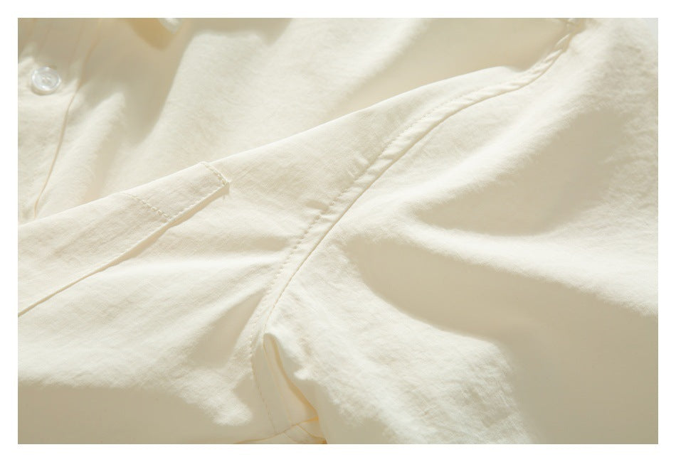 Close-up of an ivory garment’s button, placket, and overlapping stitched fabric.