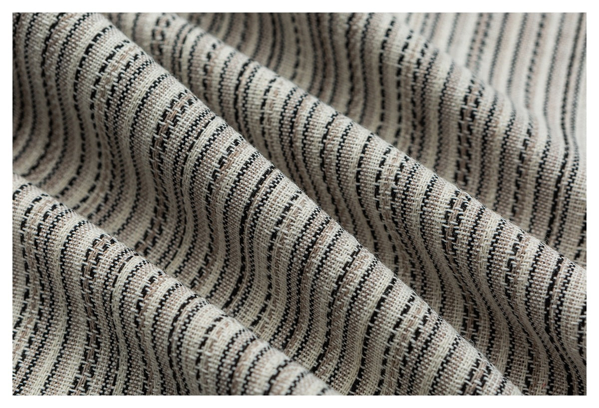 Macro view of cream, black, and gray striped fabric gathered into folds, showing its woven texture.