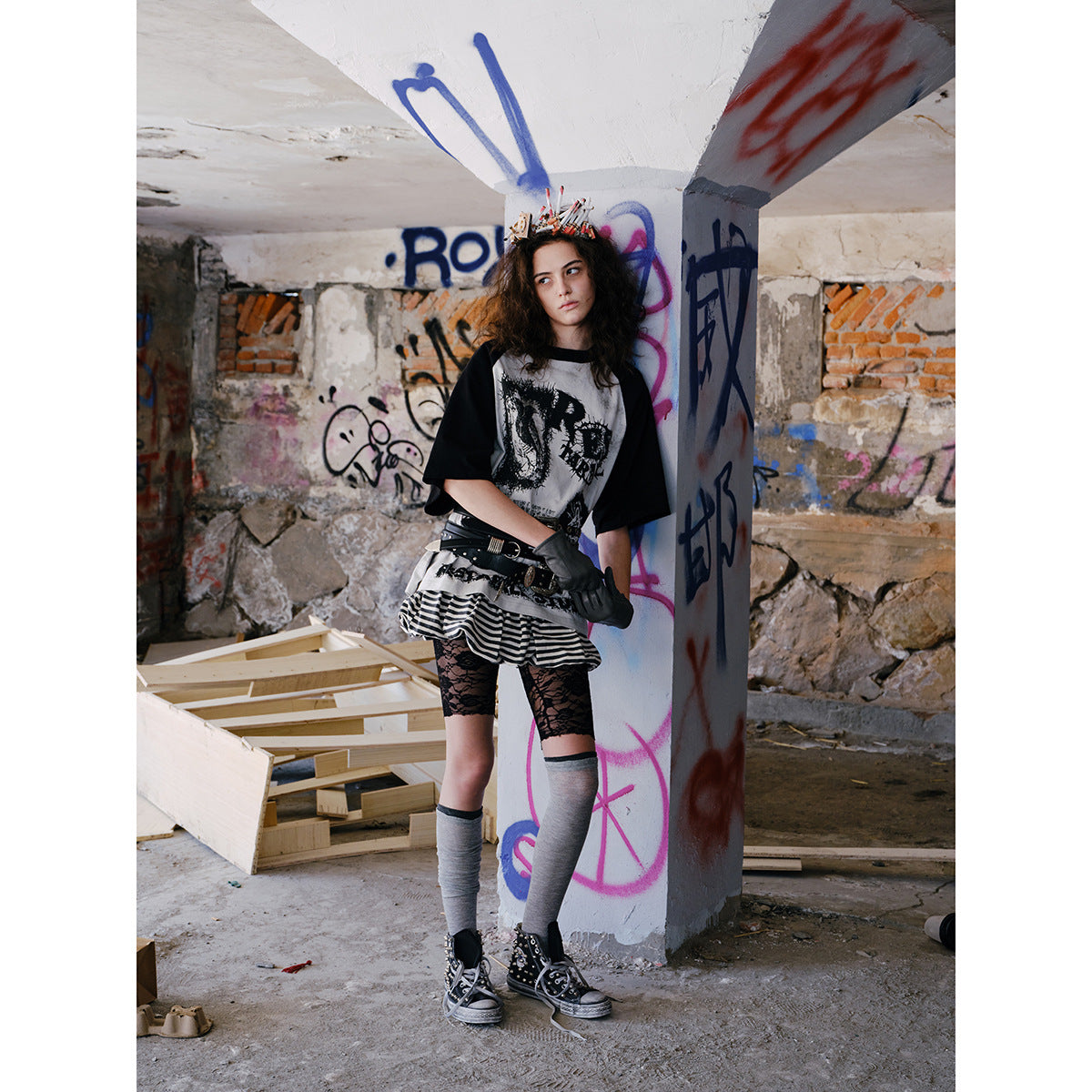 Model wears a black-and-gray graphic raglan shirt, striped skirt, lace shorts, and gray leg warmers.