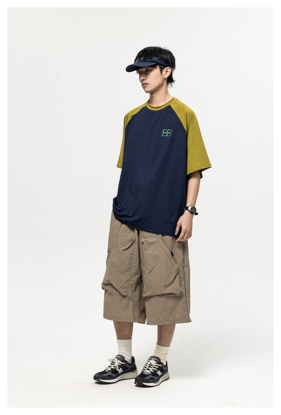 Model wearing navy short-sleeve raglan T-shirt with olive sleeves, visor, khaki wide-leg shorts and sneakers