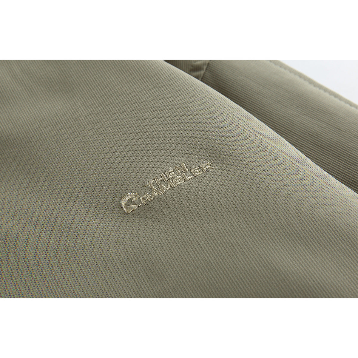 Close-up of small light-colored embroidered lettering on olive-gray jacket fabric.
