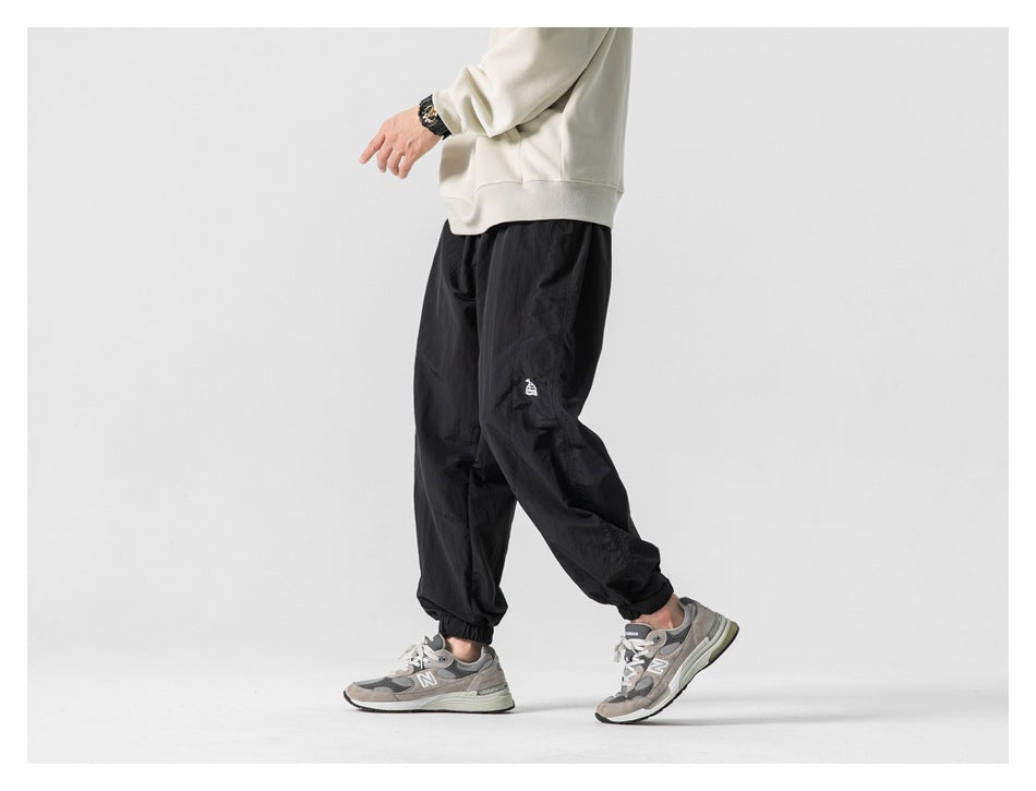 Model wearing black loose-fit jogger pants with elastic cuffs, shown from the side while walking.