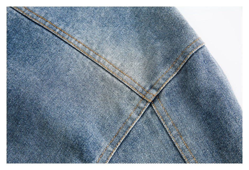 Close-up of blue denim panel seams crossing diagonally, finished with orange topstitching.