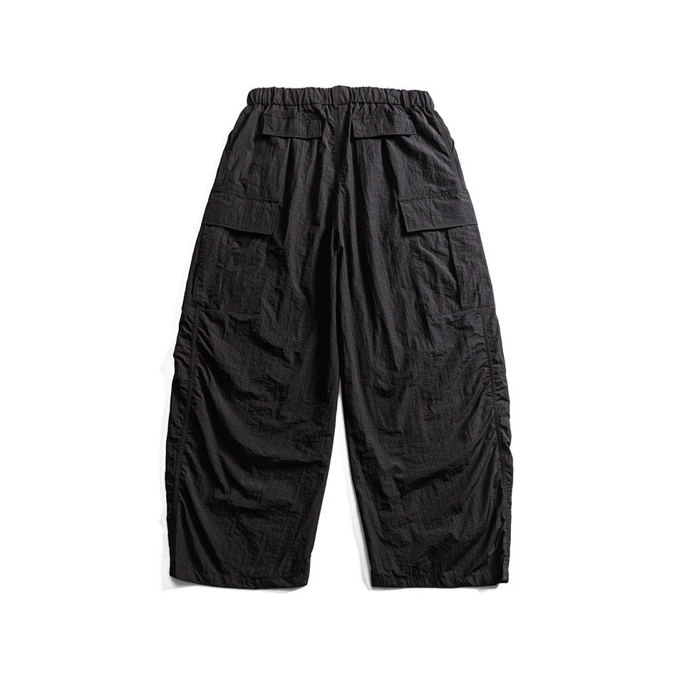 Back view of black wide-leg cargo pants with an elastic waistband and multiple flap pockets, laid flat on white.