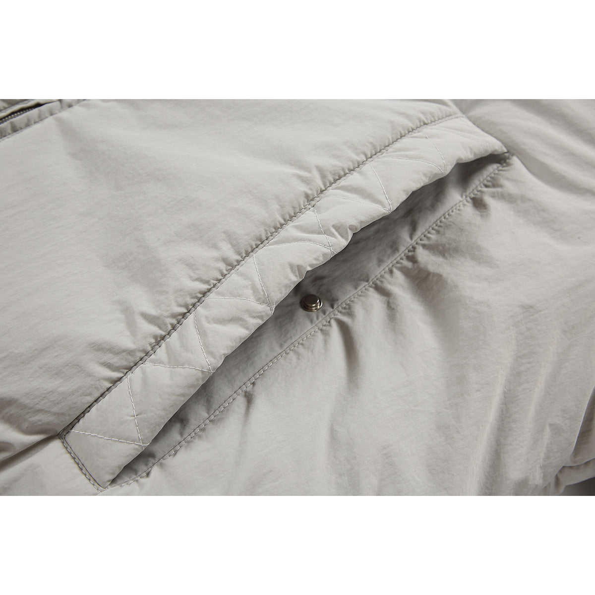 Close-up of a light gray jacket pocket flap with diamond stitching and a snap button.