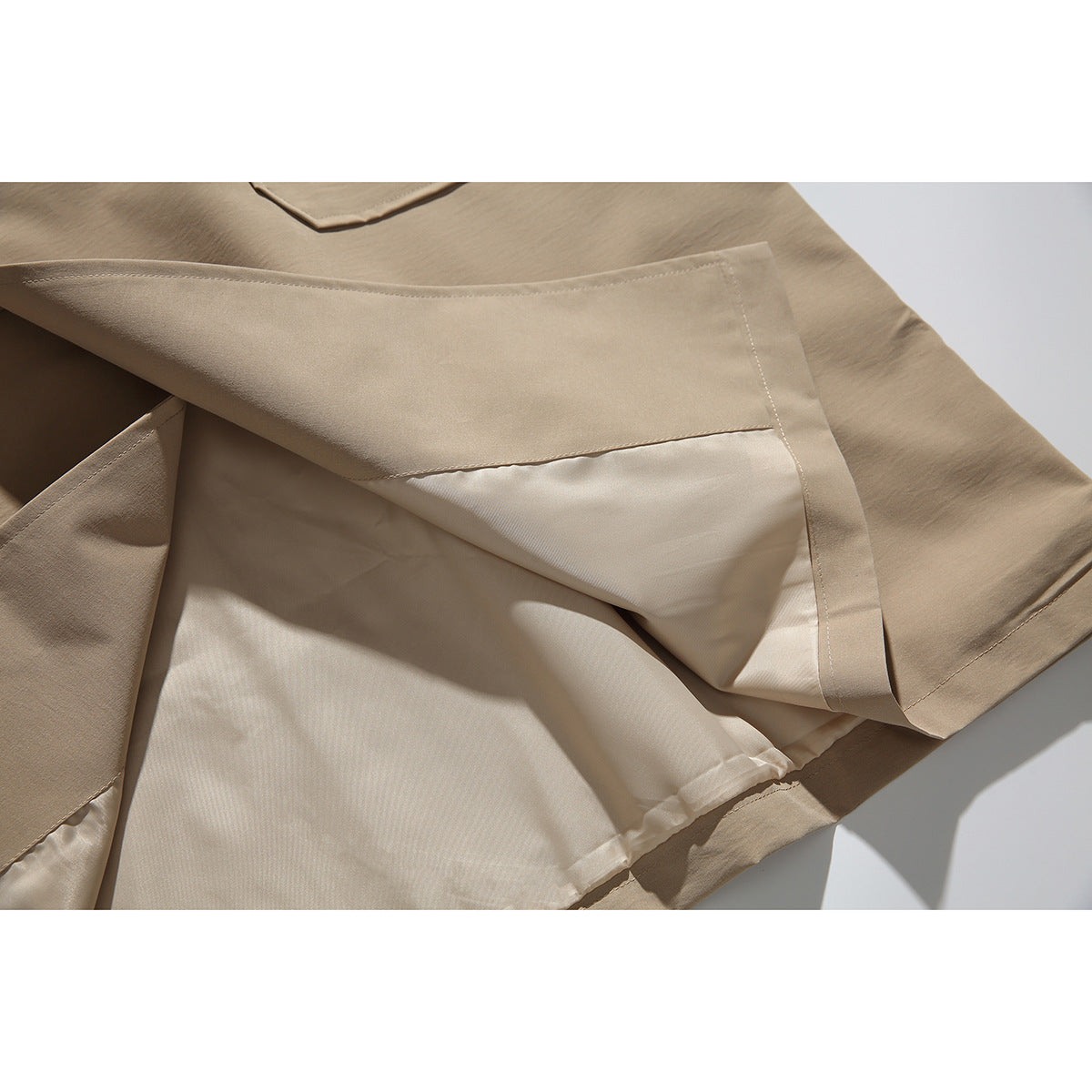 Close-up of the tan coat's hem, showing the outer fabric, lining and stitched edge.