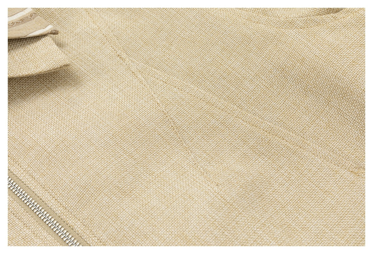 Close-up of the beige jacket's textured fabric, seam, and a section of the metal zipper.