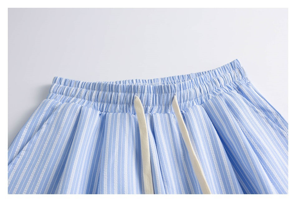 Upper front of light blue and white striped shorts with an elastic waistband and cream drawstrings.
