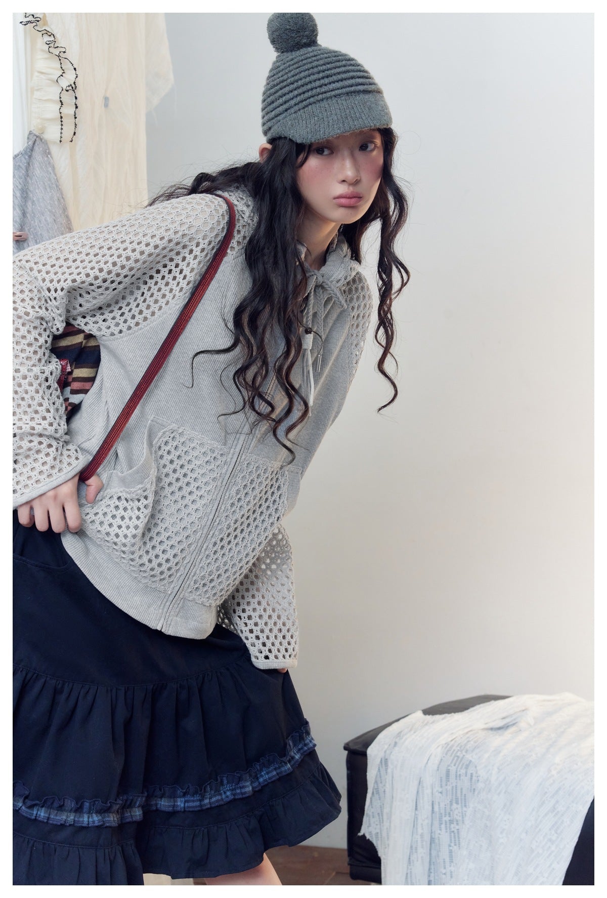 Close-up of a model wearing a light gray zip hoodie with open-knit sleeves and pockets over a navy ruffle skirt.