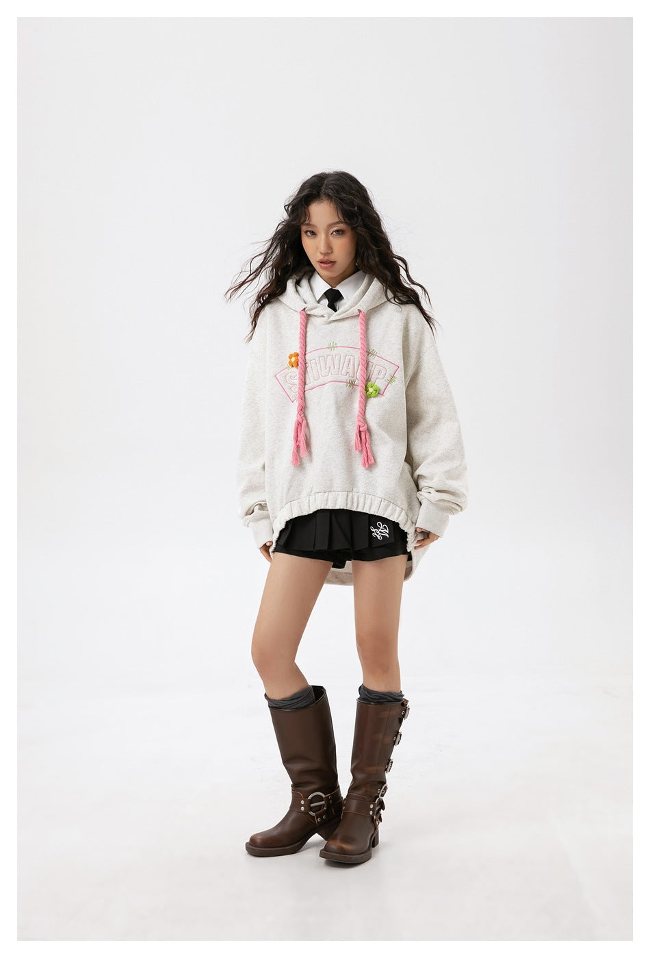 Model wearing a light gray oversized hoodie with pink braided drawstrings, black shorts and brown boots.
