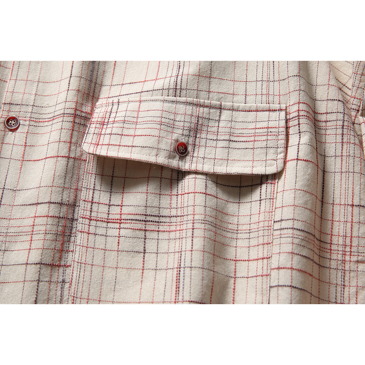 Close-up of an off-white plaid shirt's buttoned chest pocket flap and red-and-gray grid pattern.