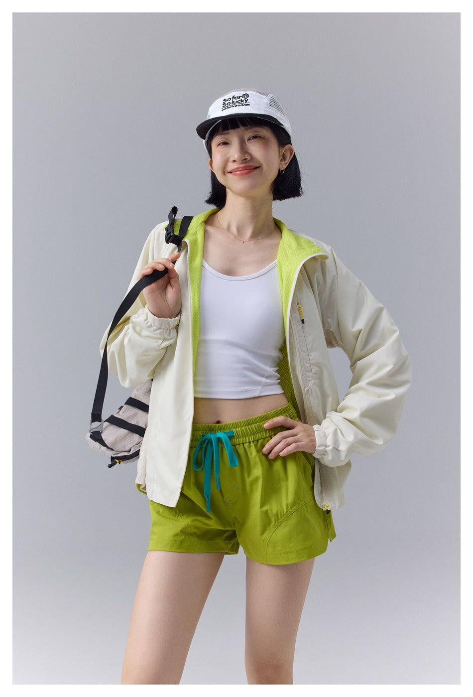 Model wearing an open off-white jacket with neon green mesh lining over a white tank top and green shorts