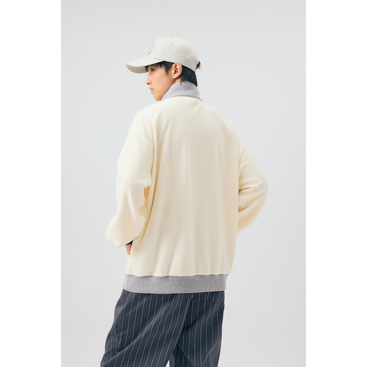 Back view of a model wearing an ivory pullover with a gray collar and hem, paired with dark striped trousers.