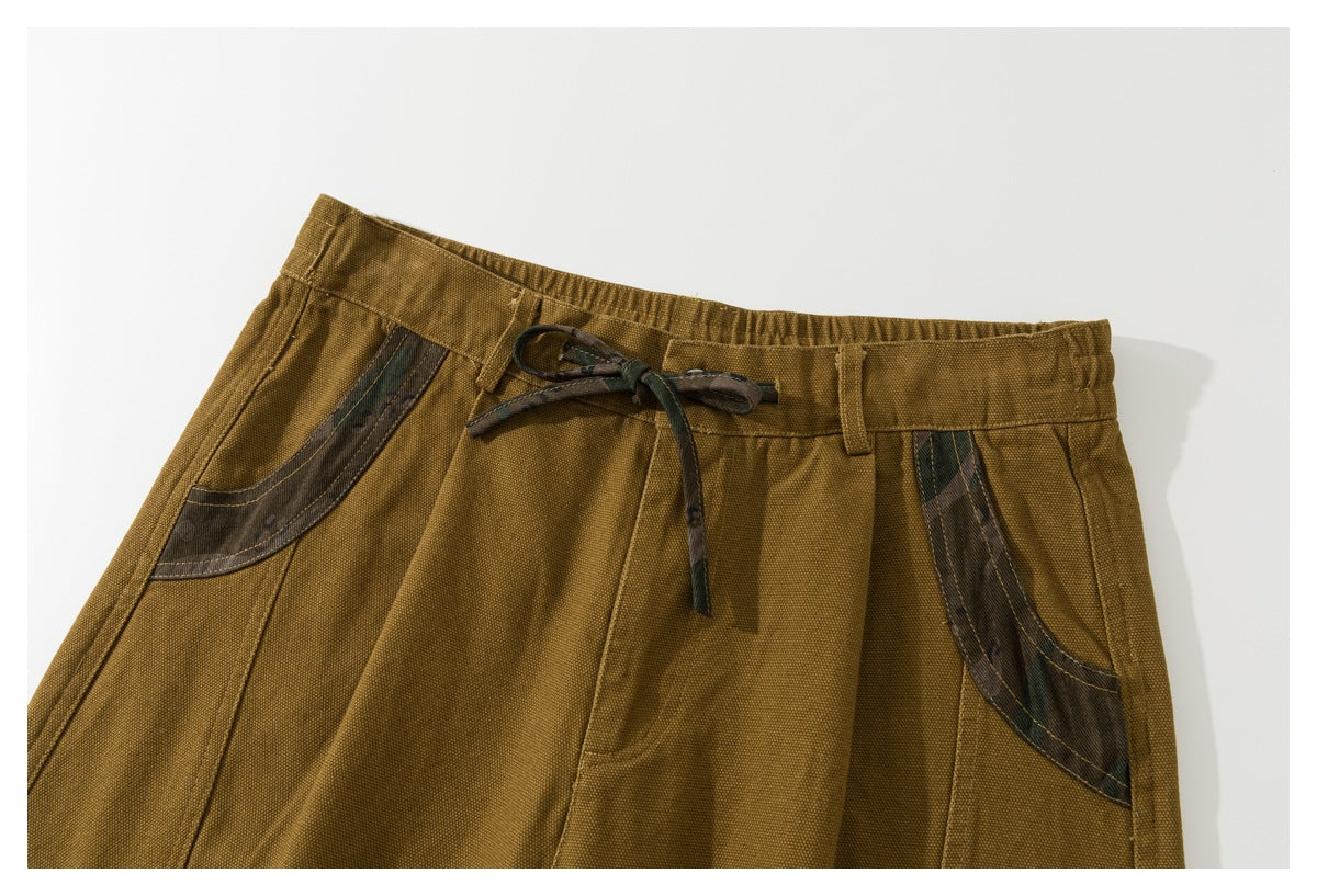 Close view of mustard-brown shorts with a drawstring waist and dark camouflage-print accents on the front pockets.