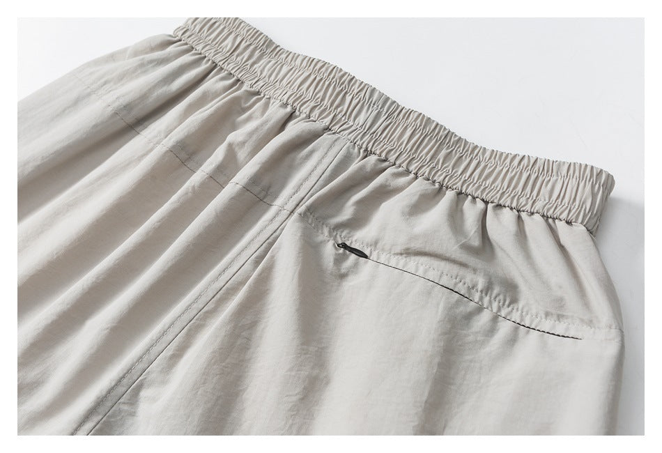 Close-up of light gray-beige pants showing the elastic waistband and a rear zip pocket.