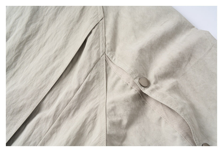 Close-up of a light beige-gray jacket pocket flap secured with a metal snap.