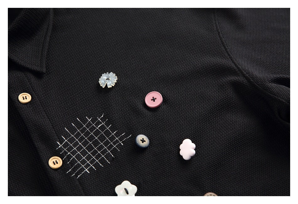 Close-up of black shirt fabric, grid stitching, and decorative buttons in varied shapes and colors.
