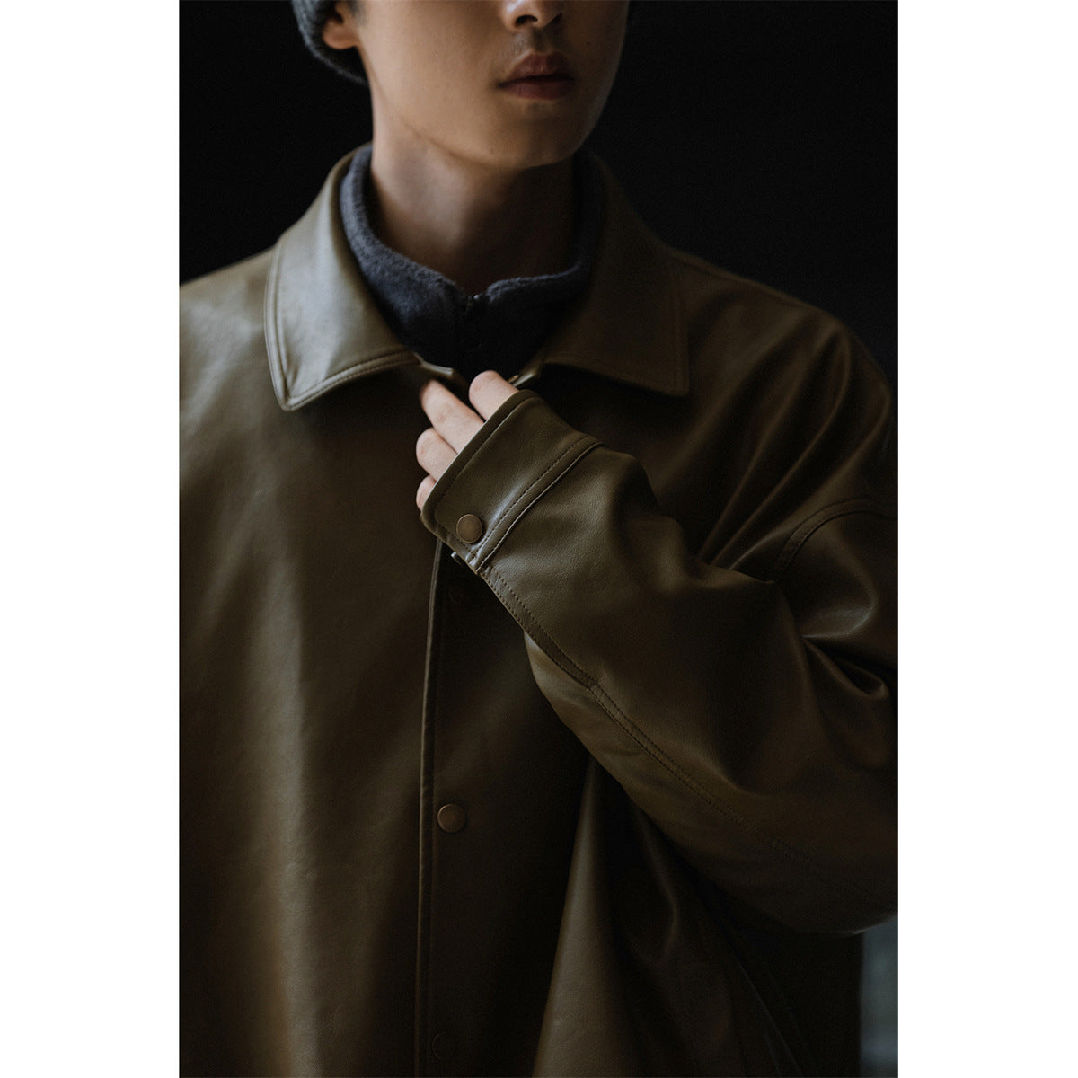 Close-up of a dark olive-brown jacket showing its pointed collar, snap-button cuff and front fasteners.