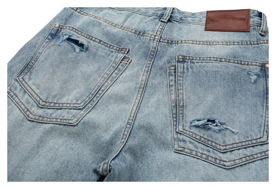 Close-up of the back of light-wash jeans with two distressed pockets and a brown waistband patch.