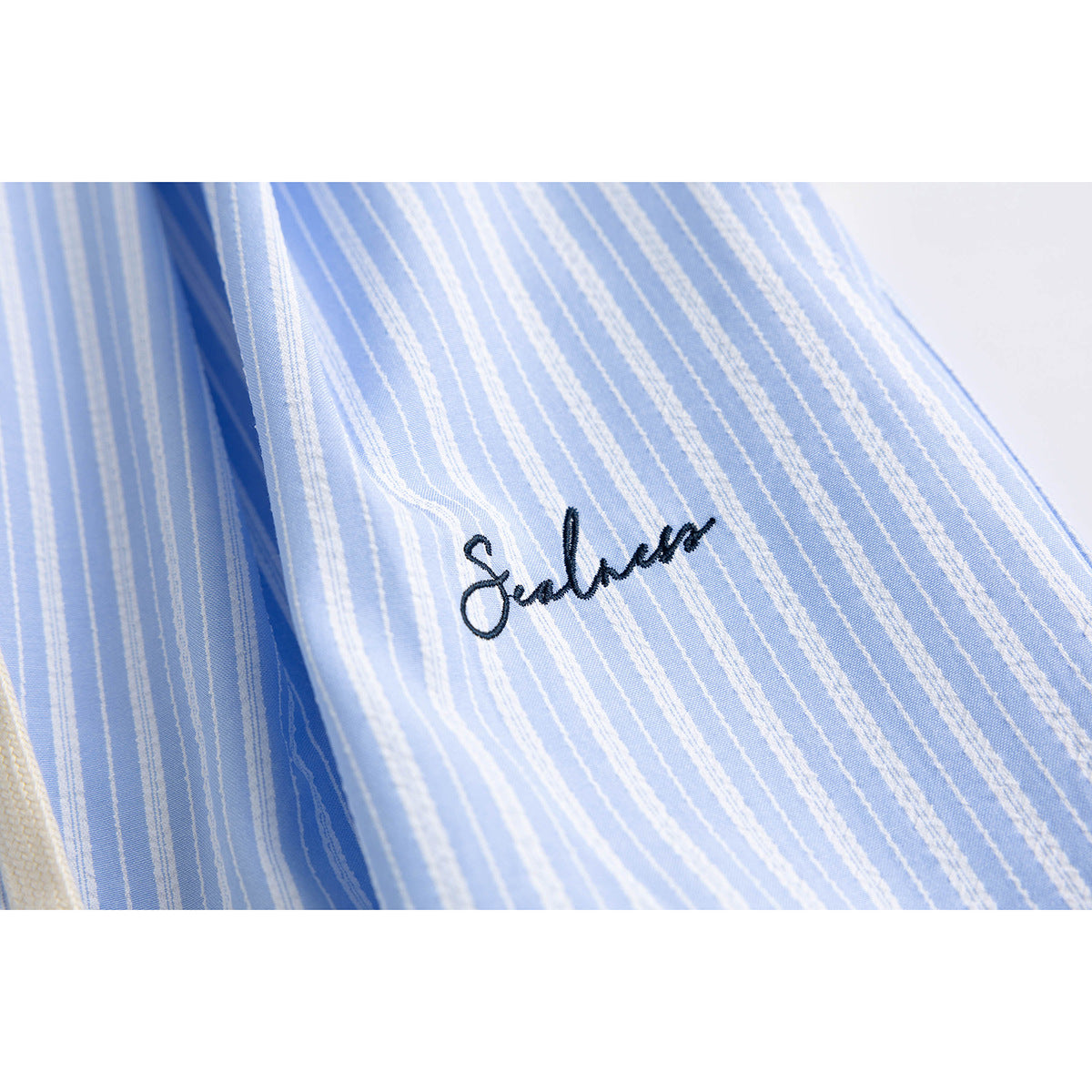 Close-up of light blue and white striped shorts with dark cursive embroidery on the fabric.