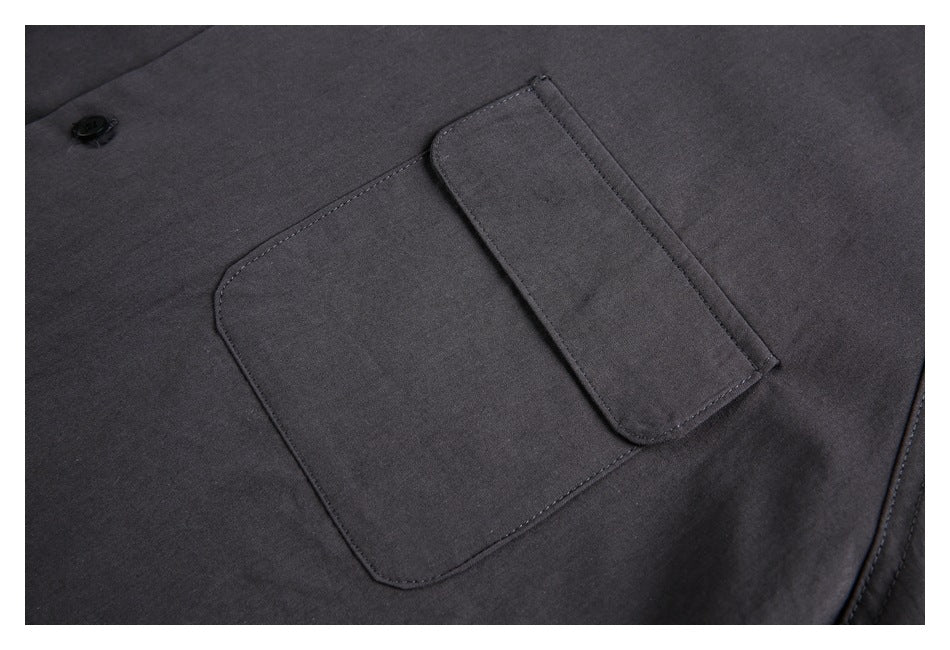 Close-up of a charcoal garment showing a flap pocket, stitching, and a black button.