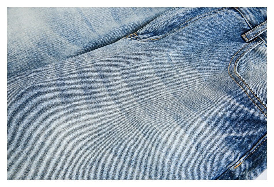 Close-up of light blue washed denim with faded texture, golden stitching, and a partial pocket and belt loop.