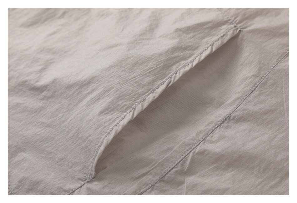 Close-up of a taupe garment showing curved seam stitching and a folded fabric panel.