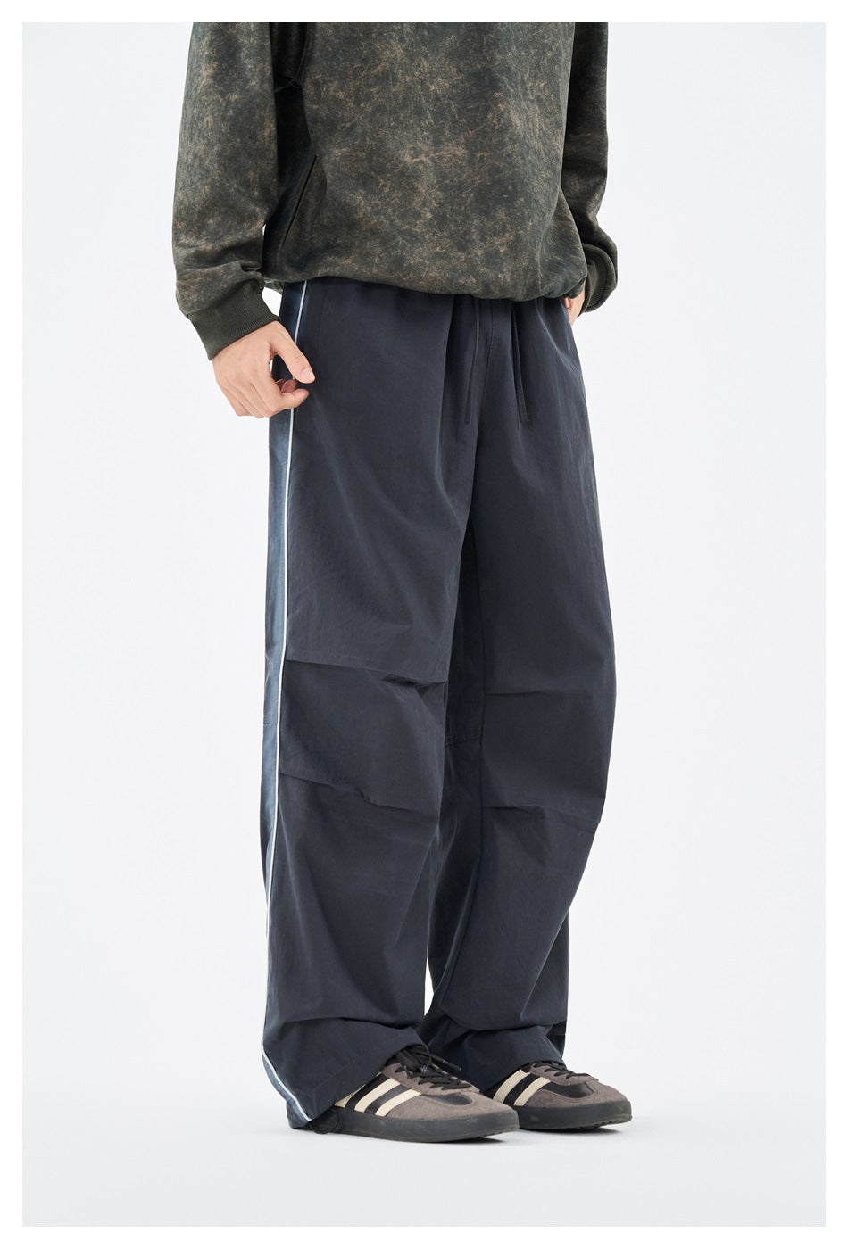 Front view of loose navy pants with a drawstring waist, paneled legs, and light side piping, worn by a model.